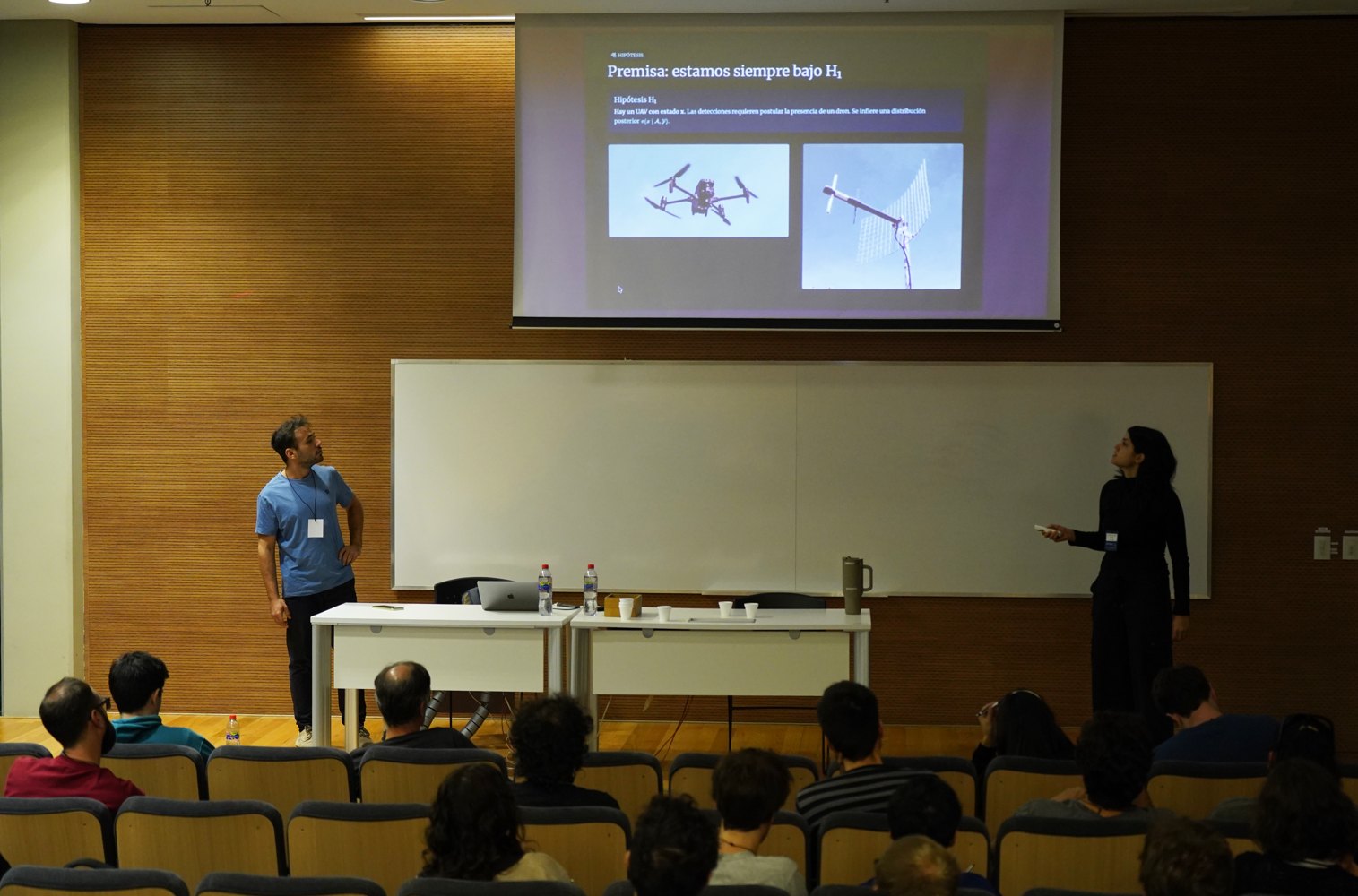 Two presenters speaking in a lecture hall during a technical presentation.